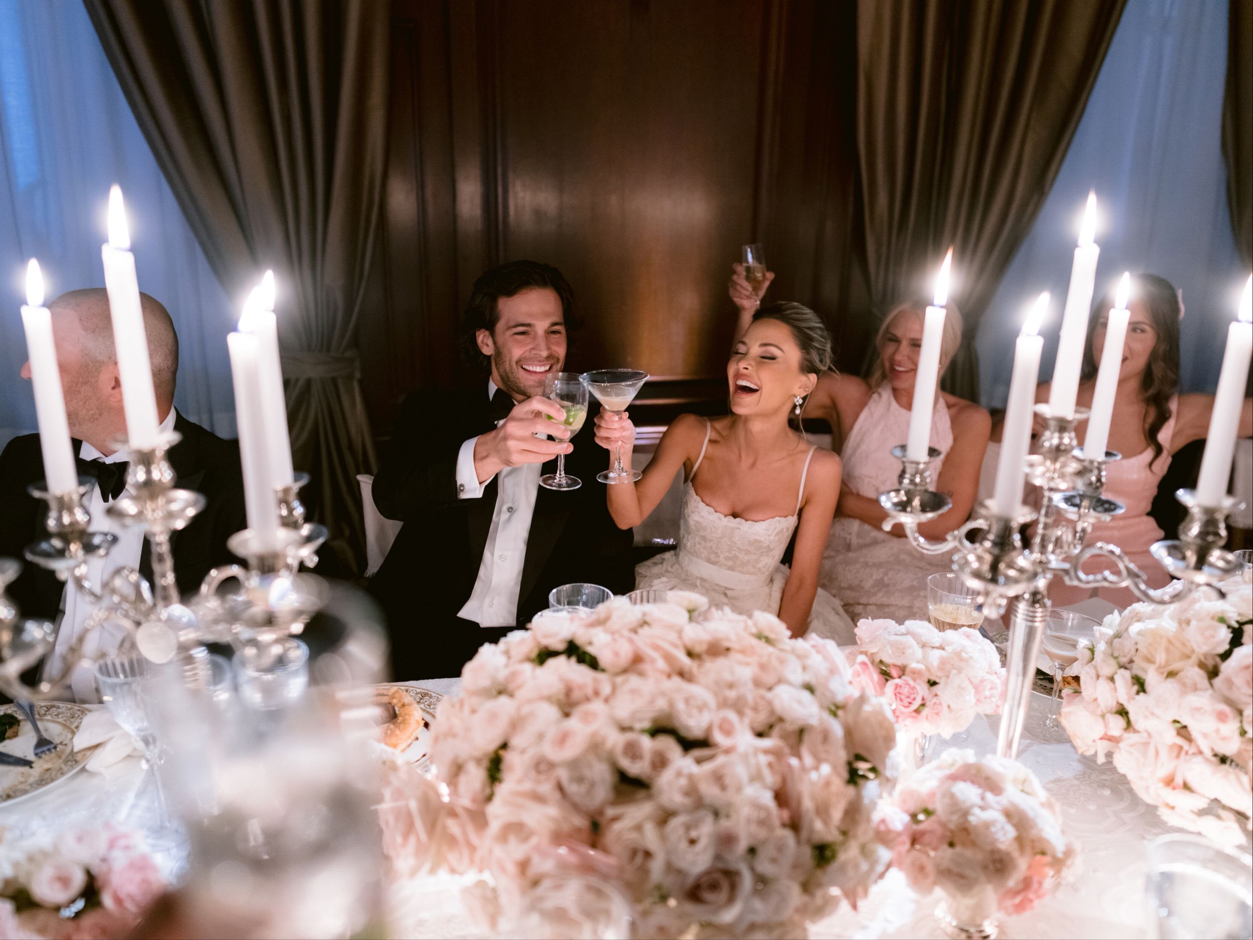 A toast at the head table, taken between candelabra and low bowls of blush roses.